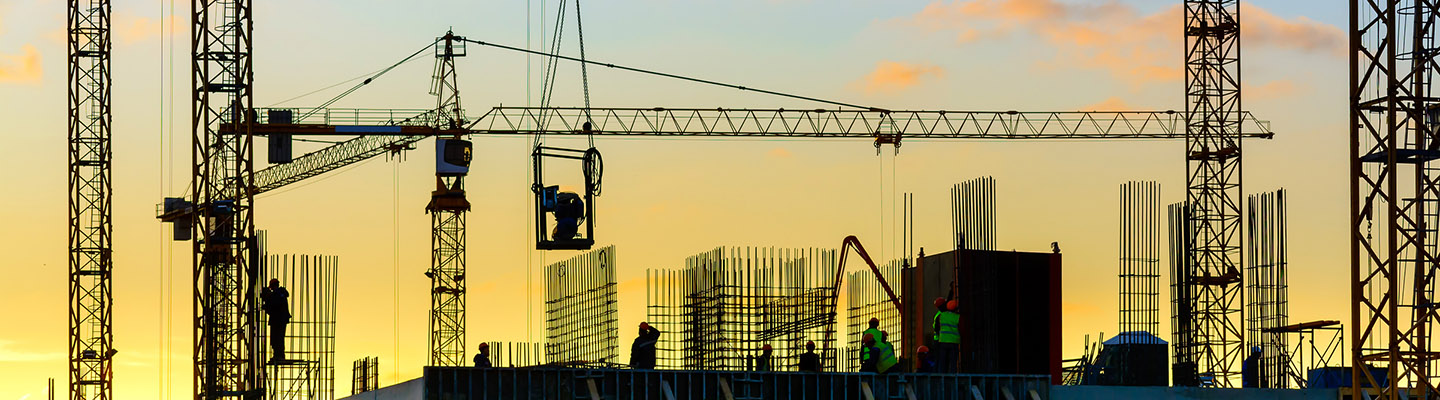 Grues à tour et la silhouette du bâtiment avec les travailleurs au coucher du soleil